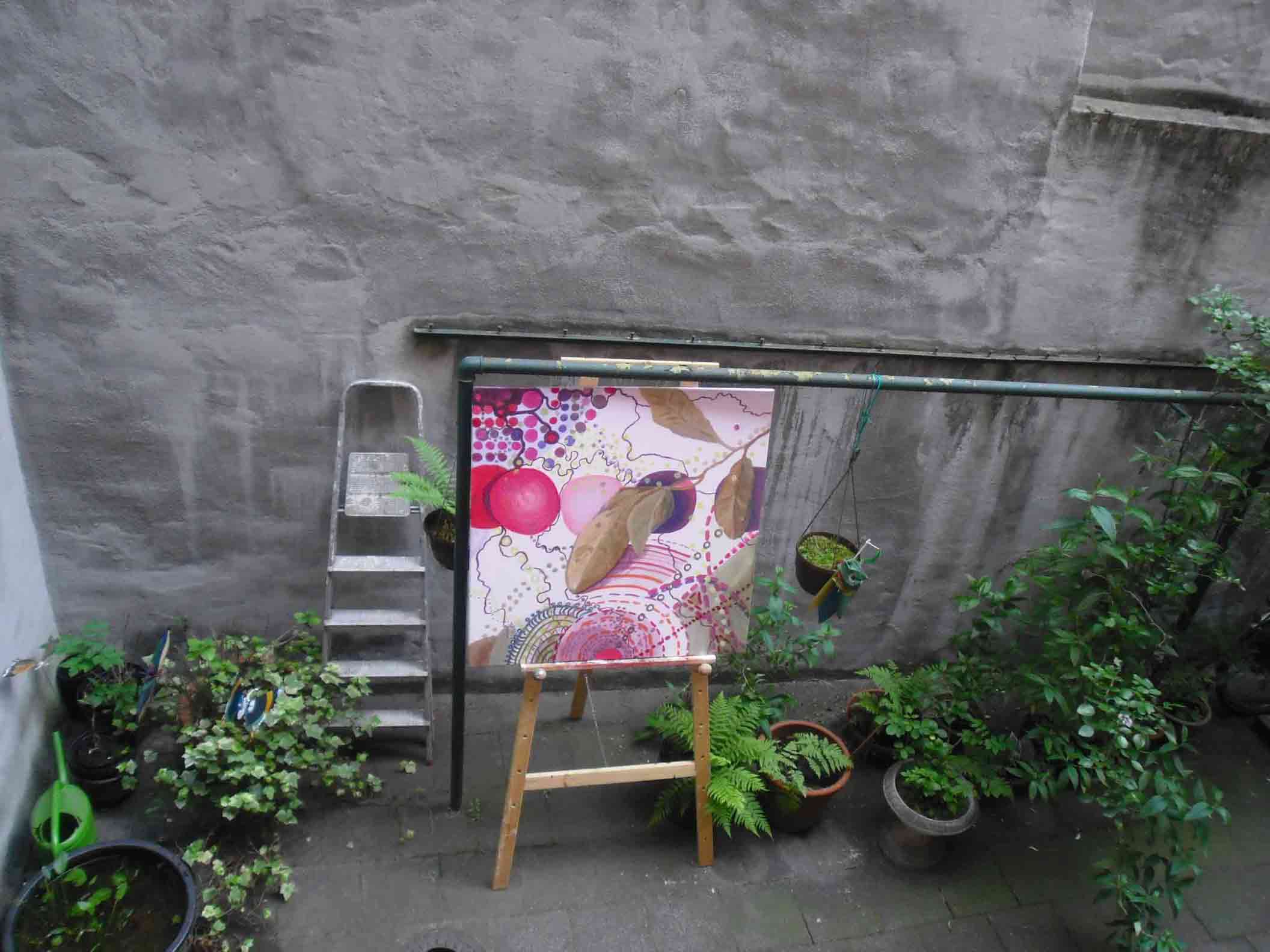 Im Innenhof auf einer Stafflei ein Bild von Kirsten zwischen Topfpflanzen